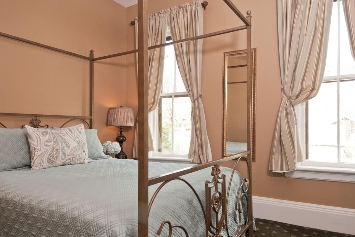 A four-poster bed with a quilted bedspread, a bedside table with a lamp, and a large mirror on the wall.