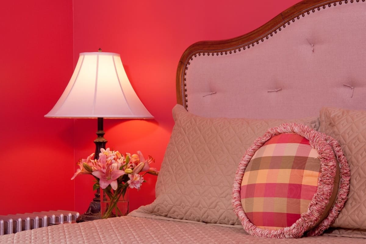 A bed with a quilted headboard, a bedside lamp, and a vase with flowers.