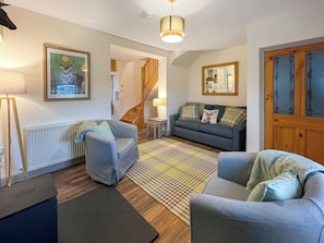 Un salon comprenant un canapé, des fauteuils, une table basse, une lampe, un tableau encadré, un radiateur, un escalier et une porte avec des panneaux de verre.