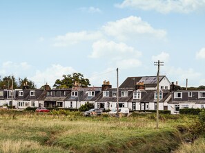 Een rij terraswoningen met een grasveld op de voorgrond en een heldere lucht.