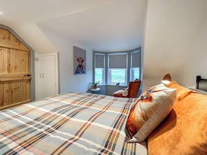 Ein Schlafzimmer mit kariertem Überwurf, einem Holzschrank, einem Fenster mit Blick und einem Bild an der Wand.