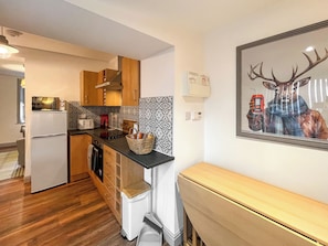 Een moderne keuken met houten kastjes, een inbouwoven en een magnetron. Er is een spoelbak, een broodrooster en een mand met snacks op het aanrecht.