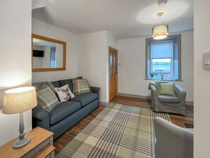 Un salon comprenant un canapé, un fauteuil plus petit, une lampe, un miroir et une fenêtre donnant sur un beau paysage.