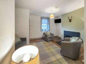 Una sala de estar con sofá, sillón y televisor montado en la pared.