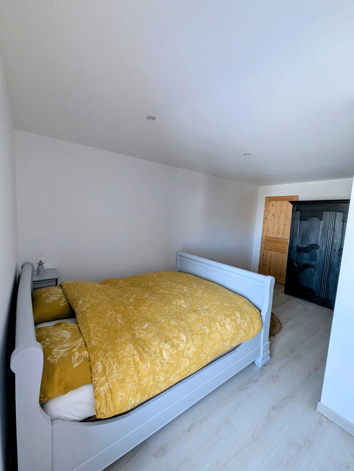 A bedroom with a single bed, a nightstand, and a wooden door.