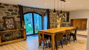 A dining area with a wooden table and chairs, stone walls, and a large window with a view of greenery. - A large 250m2 farmhouse with authentic, rustic charm, Le Repaire (Mazet-Saint-Voy)