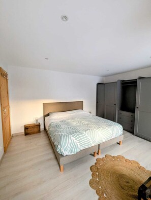 Un dormitorio con cama, mesita de noche, armario y alfombra de fibras naturales.