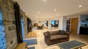 A spacious living area with a stone wall, a brown leather sofa, a wooden coffee table, and a solar-powered charger. - A large 250m2 farmhouse with authentic, rustic charm, Le Repaire (Mazet-Saint-Voy)