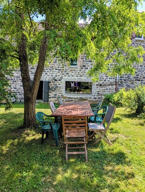 Un área de comedor al aire libre con un muro de piedra, una mesa de madera y sillas verdes.