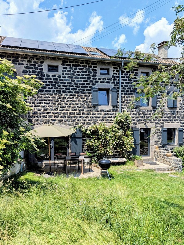 Edificio de piedra con un patio que incluye una parrilla y asientos exteriores.