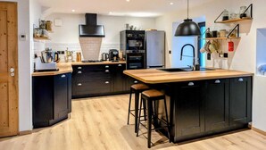 A modern kitchen with black cabinets, a wooden countertop, and a central island with stools. - A large 250m2 farmhouse with authentic, rustic charm, Le Repaire (Mazet-Saint-Voy)