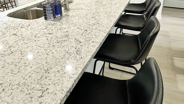 A kitchen with a granite countertop, stainless steel sink, and black bar stools. - Charming Cottage “Yellow Haus” near Gruene (New Braunfels)