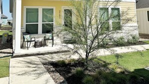 A two-story house with a front porch, a small tree in the yard, and a clear blue sky. - Charming Cottage “Yellow Haus” near Gruene (New Braunfels)