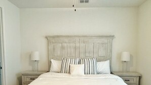 A bedroom with a large bed, two bedside tables, a ceiling fan, and a light fixture. - Charming Cottage “Yellow Haus” near Gruene (New Braunfels)