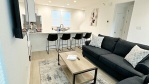 A modern living room with a black sofa, a coffee table, and a ceiling fan. - Charming Cottage “Yellow Haus” near Gruene (New Braunfels)