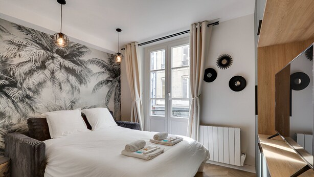 Ein modernes Schlafzimmer mit einem großen Bett, einem Fenster mit Vorhängen, einer Heizung und Wanddekorationen, darunter Schallplatten.