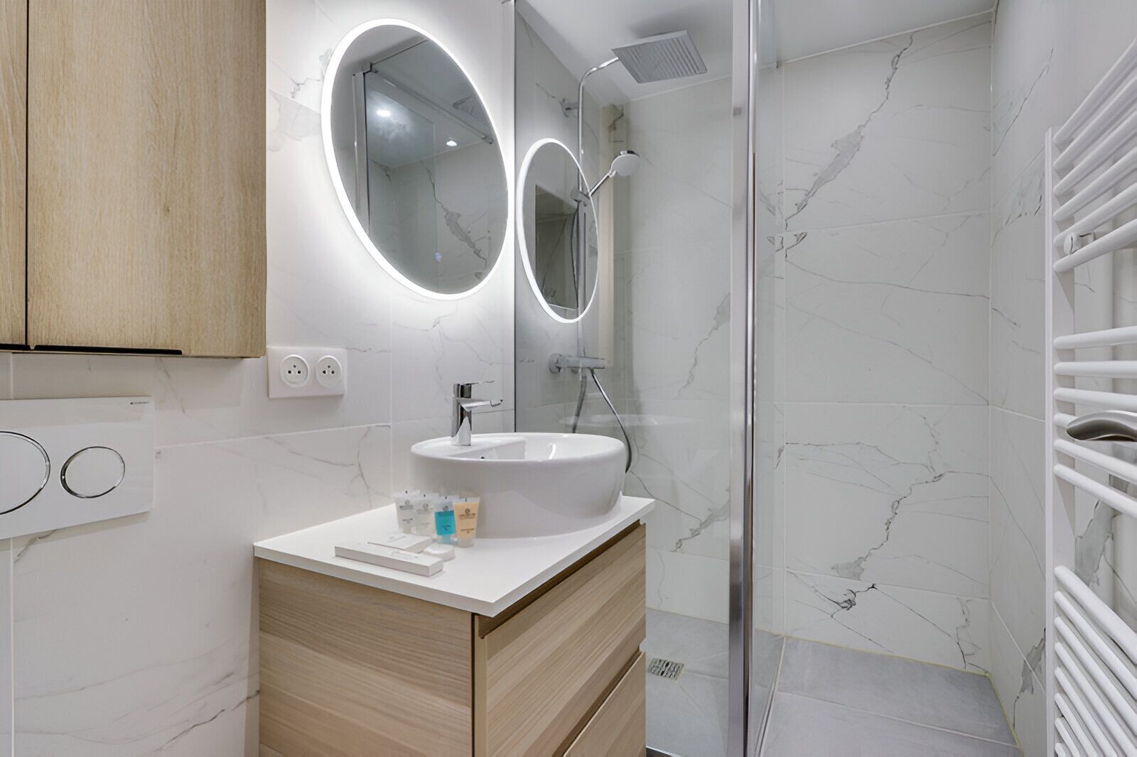 Een moderne badkamer met een witte marmeren wastafel, houten kastjes en een douchecabine van glas.