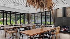 A spacious dining area with large windows, a fireplace, and bamboo chairs. - Privately Managed Golf View - Bangalay Villas (Shoalhaven Heads)