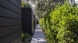 A narrow pathway flanked by dense greenery and a dark-colored building facade. - Privately Managed Golf View - Bangalay Villas (Shoalhaven Heads)