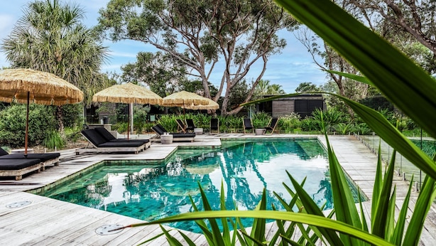 A pool area with wooden decking, lounge chairs, and thatched umbrellas. - Privately Managed Golf View - Bangalay Villas (Shoalhaven Heads)