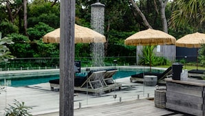 A poolside area with a wooden deck, lounge chairs, and thatched umbrellas. - Privately Managed Golf View - Bangalay Villas (Shoalhaven Heads)