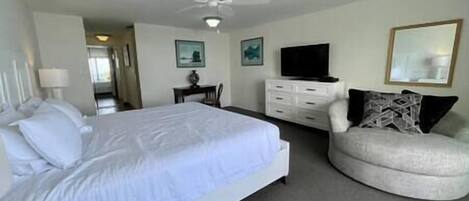 Una habitación de hotel con una cama, una silla, un televisor y un ventilador de techo.