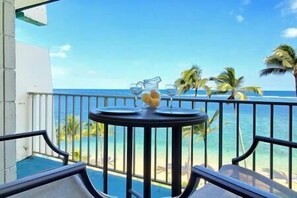 A balcony with a table set for two, overlooking a pool and a beach with palm trees. - Coastal Dream Getaway 4 (Hauula)