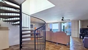 A spacious living area with a curved staircase, a large window, and a balcony.