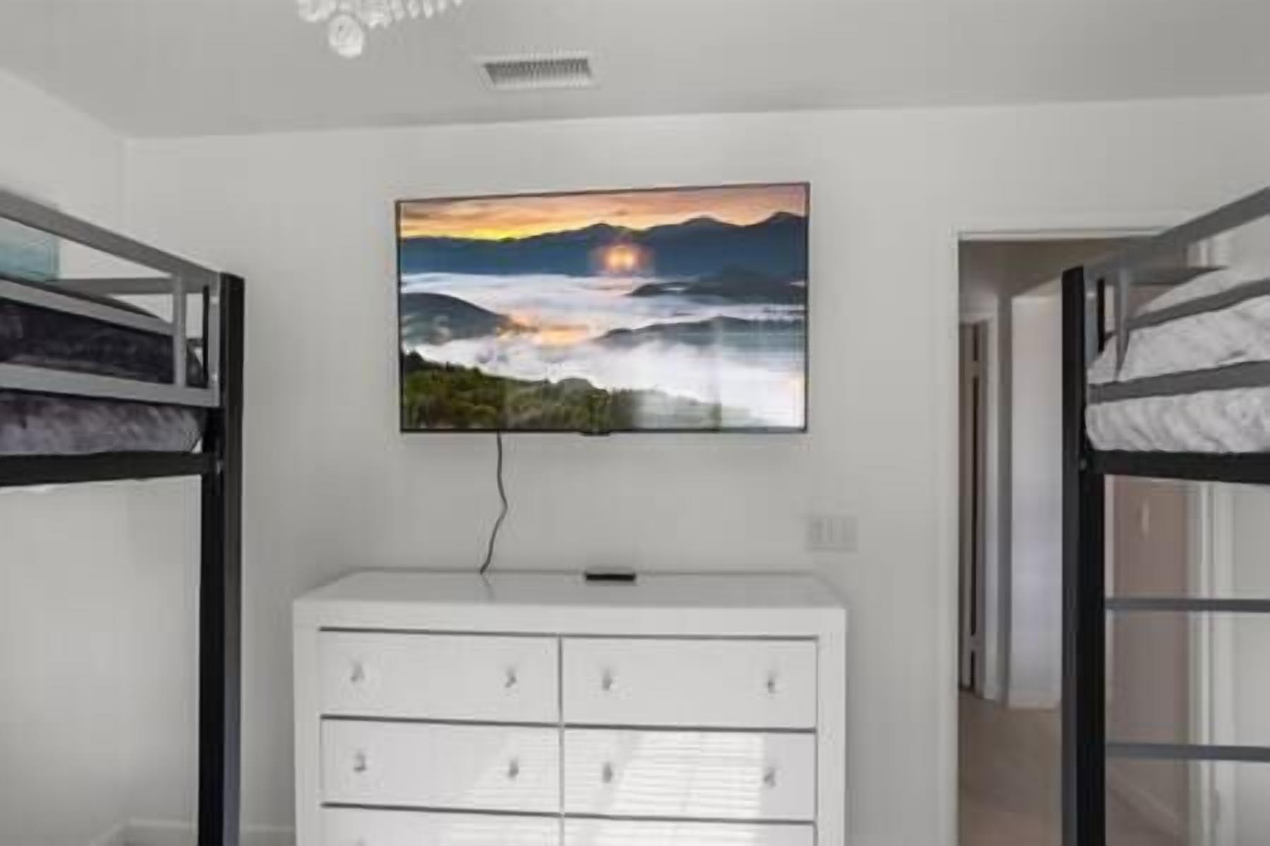 Un dormitorio con literas, un aparador blanco y un televisor de pared que muestra un paisaje pintoresco.