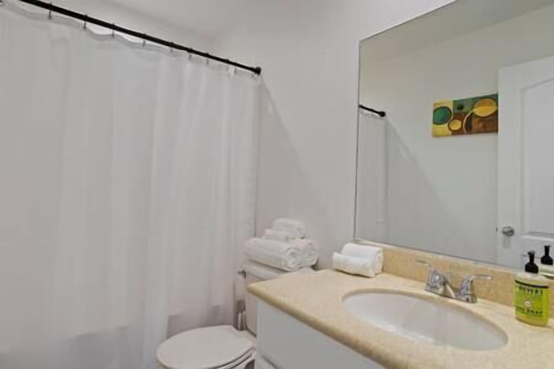 A bathroom with a shower curtain, a toilet, a sink with a mirror, and a towel rack.