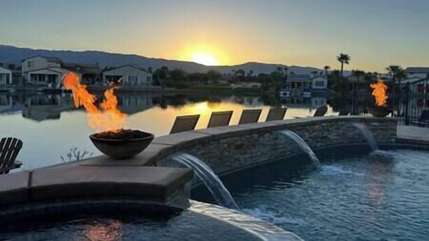 Une piscine agrémentée d’une cascade, avec un coucher de soleil en arrière-plan.