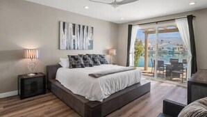 Une chambre avec un grand lit, un ventilateur de plafond et une vue sur une piscine, visible à travers une porte vitrée.