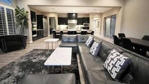 A modern living room with a sectional sofa, a small coffee table, and a dining area with a table and chairs. - Luxe Desert Oasis: Pool, Spa, Gym & Golf Cart Access Champ (La Quinta)