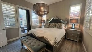 A bedroom with a large bed, a bench, a chandelier, and a nightstand. - Luxe Desert Oasis: Pool, Spa, Gym & Golf Cart Access Champ (La Quinta)