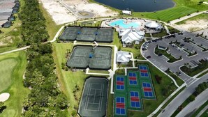 Vista aérea de un campo de golf con varias canchas de tenis, piscina y zona de estacionamiento.