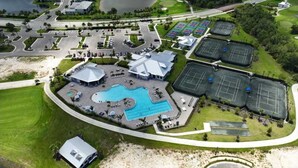 Vista aérea de un complejo turístico con piscina, canchas de tenis y aparcamiento.