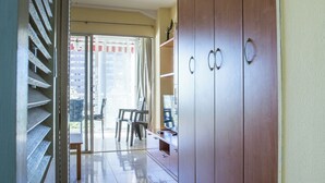 A room with a sliding glass door leading to a balcony, a wooden wardrobe, and a small table with chairs.