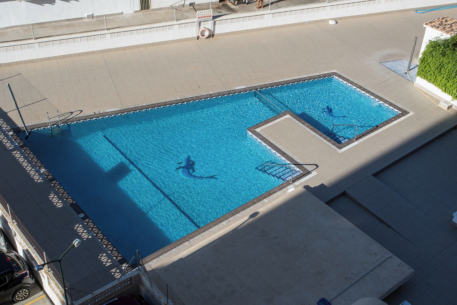 Uma piscina ao ar livre com água azul cristalina, um trampolim e uma cadeira salva-vidas.