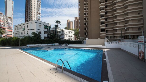 An outdoor swimming pool surrounded by high-rise buildings, with a clear sky above.
