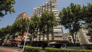 A multi-story building with balconies, surrounded by trees and various storefronts.