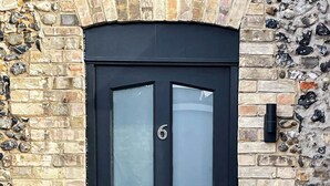 A black double door with a glass panel, set in a stone wall with a number '6' visible on the door. - Thetford Hive (Thetford)