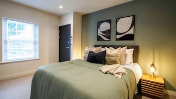 A bedroom with a bed, a nightstand, a window with blinds, and two wall-mounted abstract paintings.