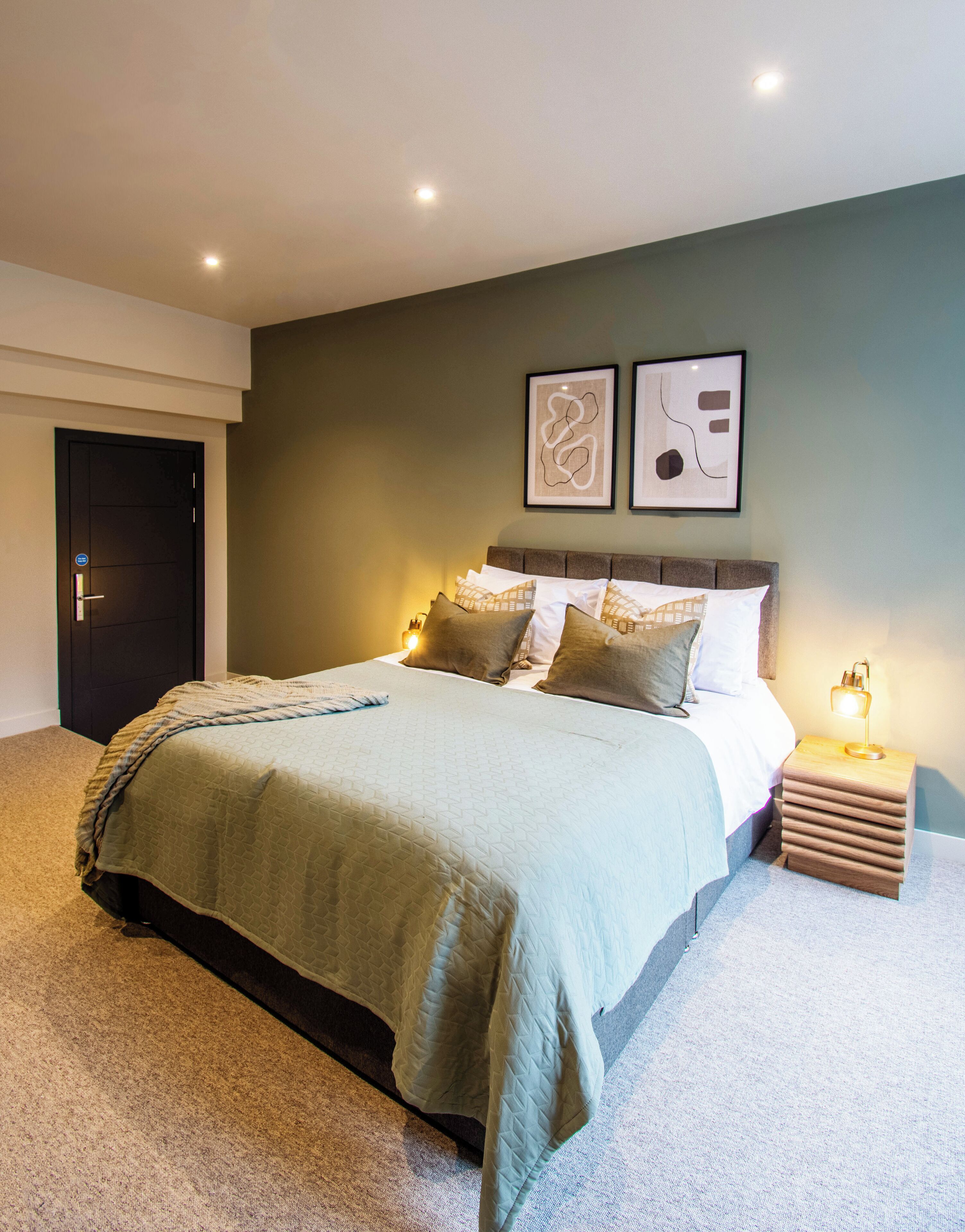 A modern bedroom with a large bed, a nightstand with a lamp, and two framed abstract artworks on the wall.