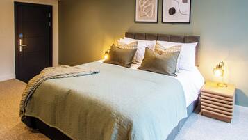 A modern bedroom with a large bed, a nightstand with a lamp, and two framed abstract artworks on the wall.