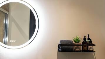 A bathroom with a round mirror, a towel, a plant, and toiletries on a shelf.