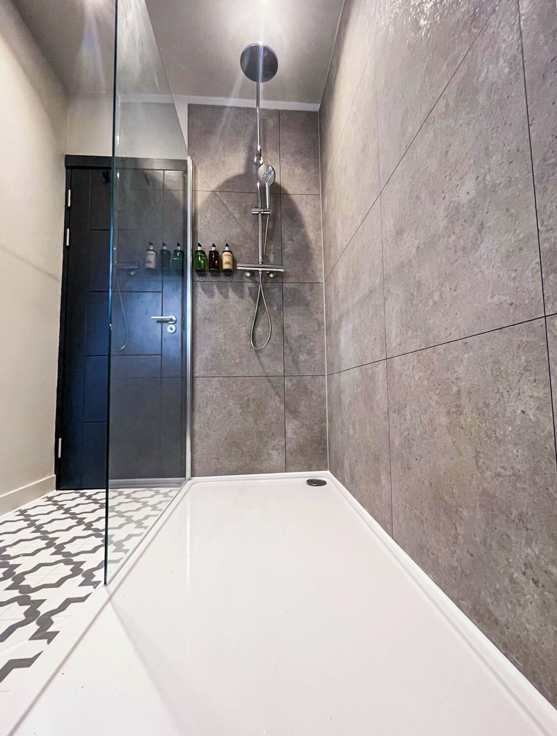 A modern shower area with a glass door, a showerhead, and a shelf with toiletries.