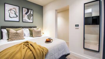 Un dormitorio con cama, almohadas, un edredón, una mesita de noche con una vela y un aire acondicionado instalado en la pared.