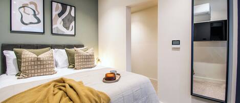 Un dormitorio con cama, almohadas, un edredón, una mesita de noche con una vela y un aire acondicionado instalado en la pared.