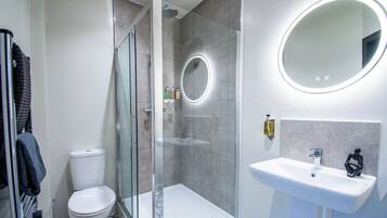Et moderne badeværelse med et glasafskærmet brusebad, en hvid vask med et rundt spejl og et toilet.