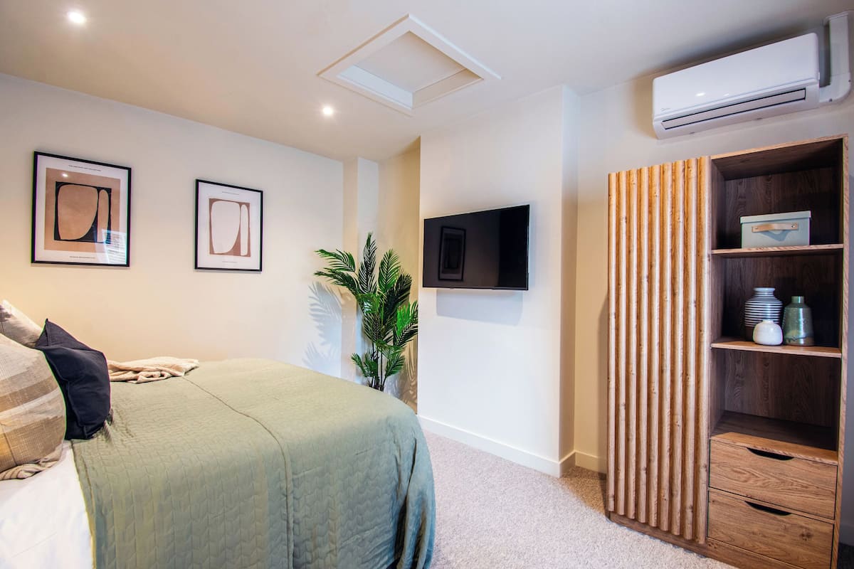 Un dormitorio con cama, televisor montado en la pared, aire acondicionado y armario de madera.